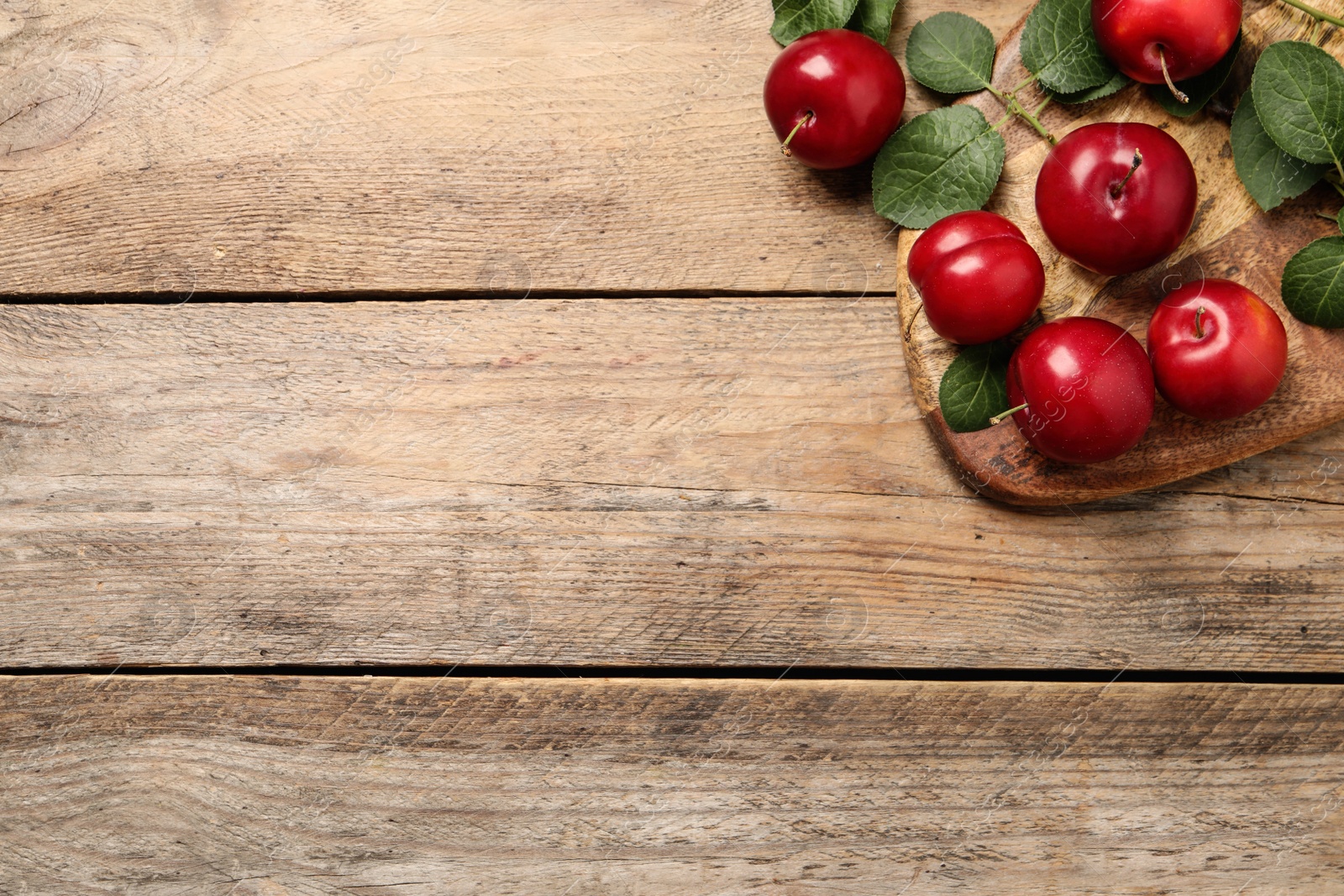 Photo of Delicious ripe cherry plums with leaves on wooden table, flat lay. Space for text