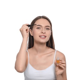 Photo of Young woman applying oil onto her eyebrows on white background