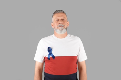Photo of Mature man with blue ribbon on grey background. Urological cancer awareness