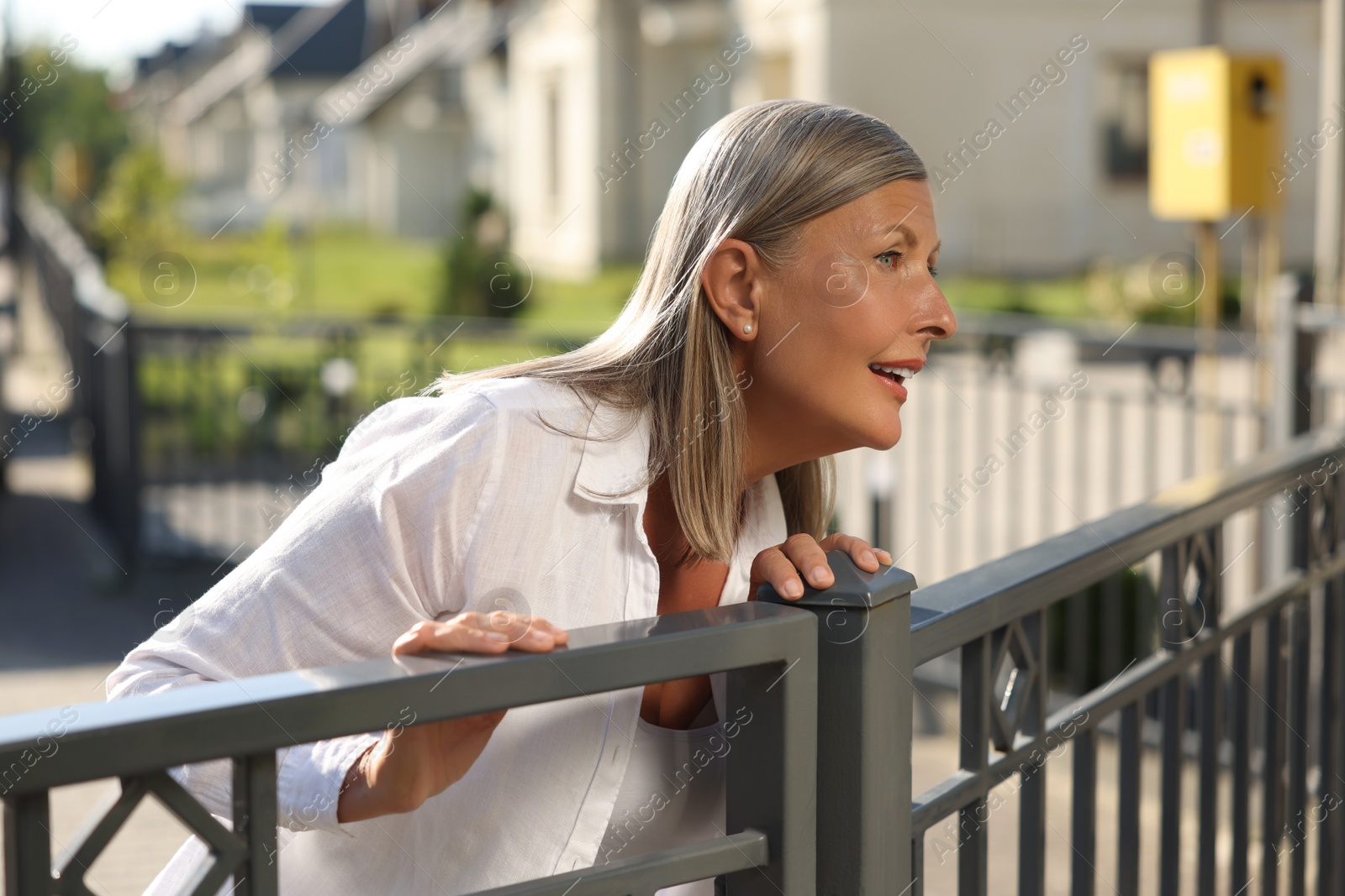 Photo of Concept of private life. Curious senior woman spying on neighbours over fence outdoors