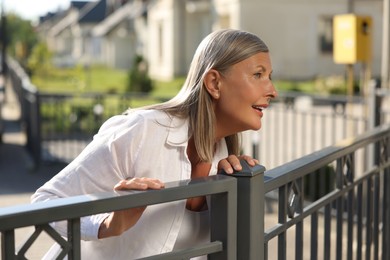 Photo of Concept of private life. Curious senior woman spying on neighbours over fence outdoors