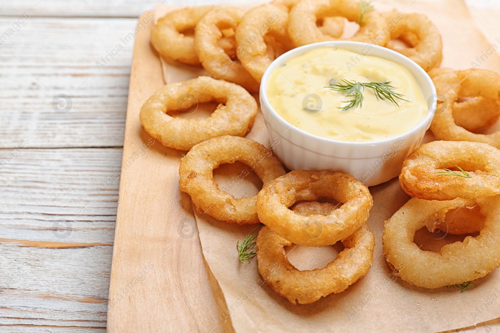 Photo of Fried onion rings served with sauce on wooden board, closeup