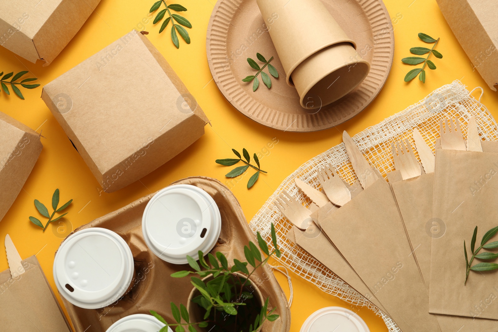 Photo of Paper and wooden tableware with green twigs on yellow background, flat lay. Eco friendly lifestyle