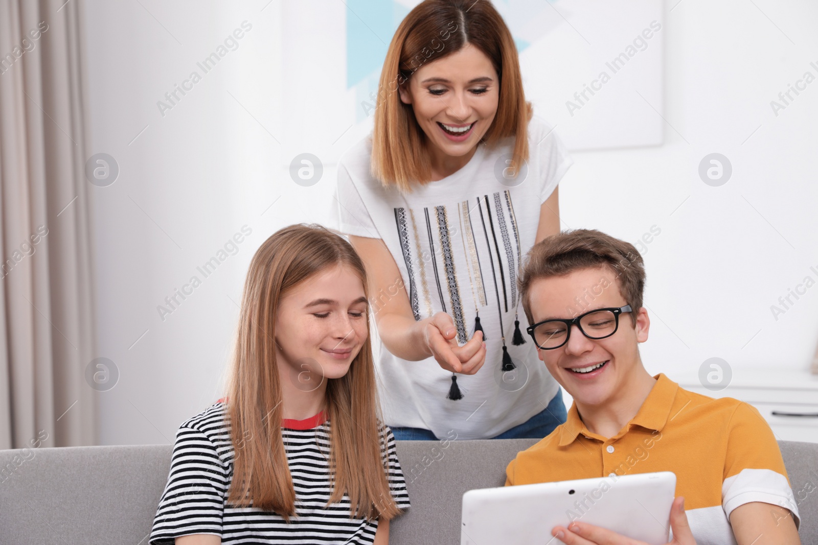 Photo of Happy mother, her teenager daughter and son with tablet at home