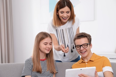 Photo of Happy mother, her teenager daughter and son with tablet at home