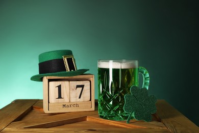 Photo of St. Patrick's day celebrating on March 17. Green beer, block calendar, leprechaun hat and decorative clover leaf on wooden table