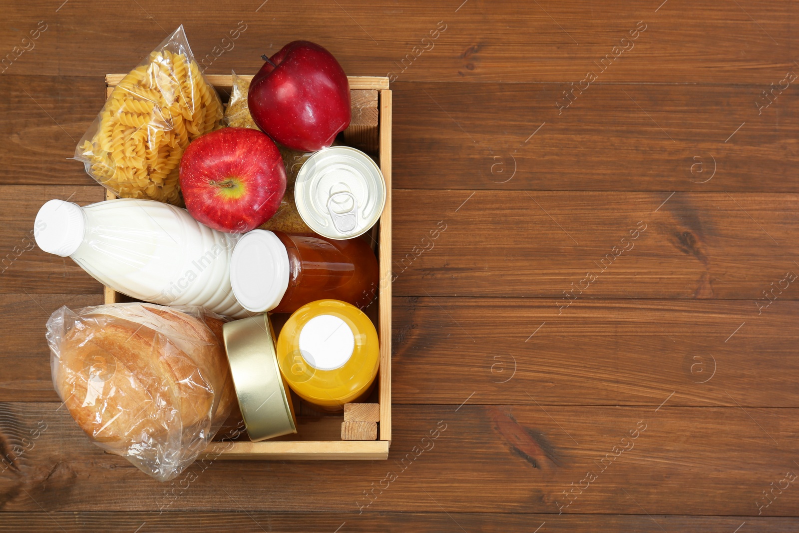 Photo of Humanitarian aid. Different food products for donation in crate on wooden table, top view. Space for text