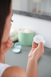 Photo of Young woman holding cotton pad with fallen eyelashes indoors