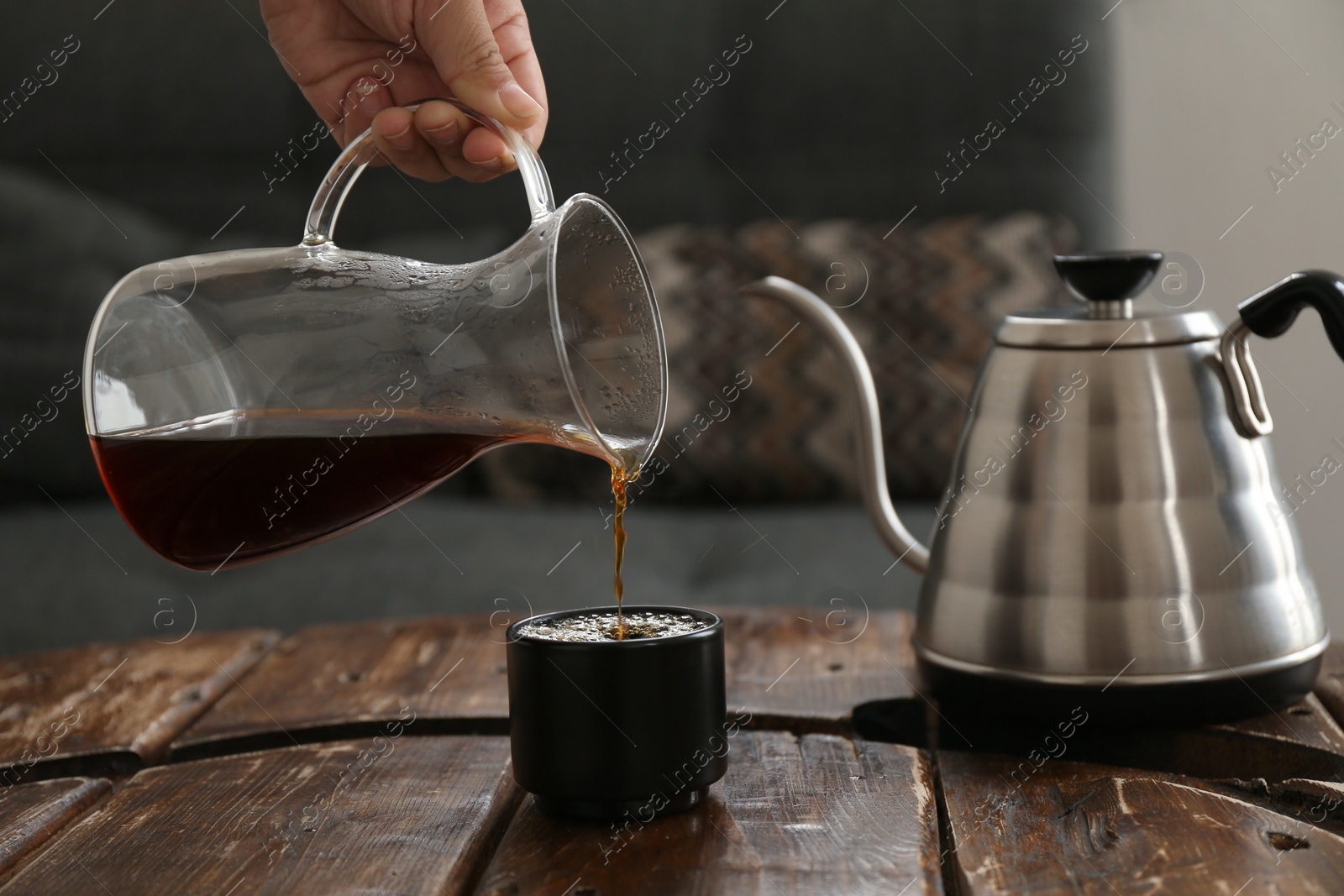 Photo of Barista pouring coffee into cup at wooden table in cafe, closeup