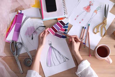 Photo of Fashion designer drawing sketch at wooden table, top view