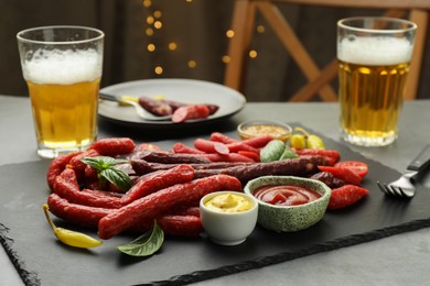 Different thin dry smoked sausages, sauces and glasses of beer on grey table