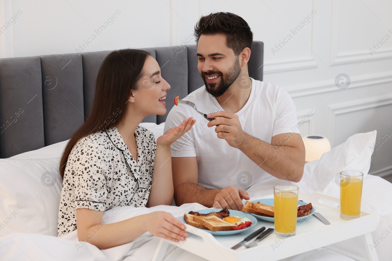 Photo of Happy couple having breakfast on bed at home