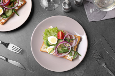Photo of Tasty sandwich with ham and quail eggs served on grey table, flat lay
