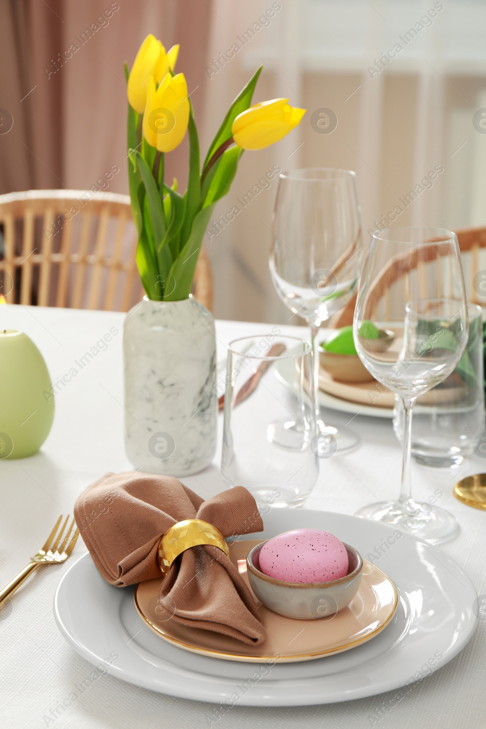 Photo of Festive Easter table setting with painted egg, burning candle and yellow tulips indoors