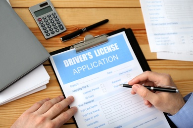 Man filling in driver's license application form at wooden table, top view