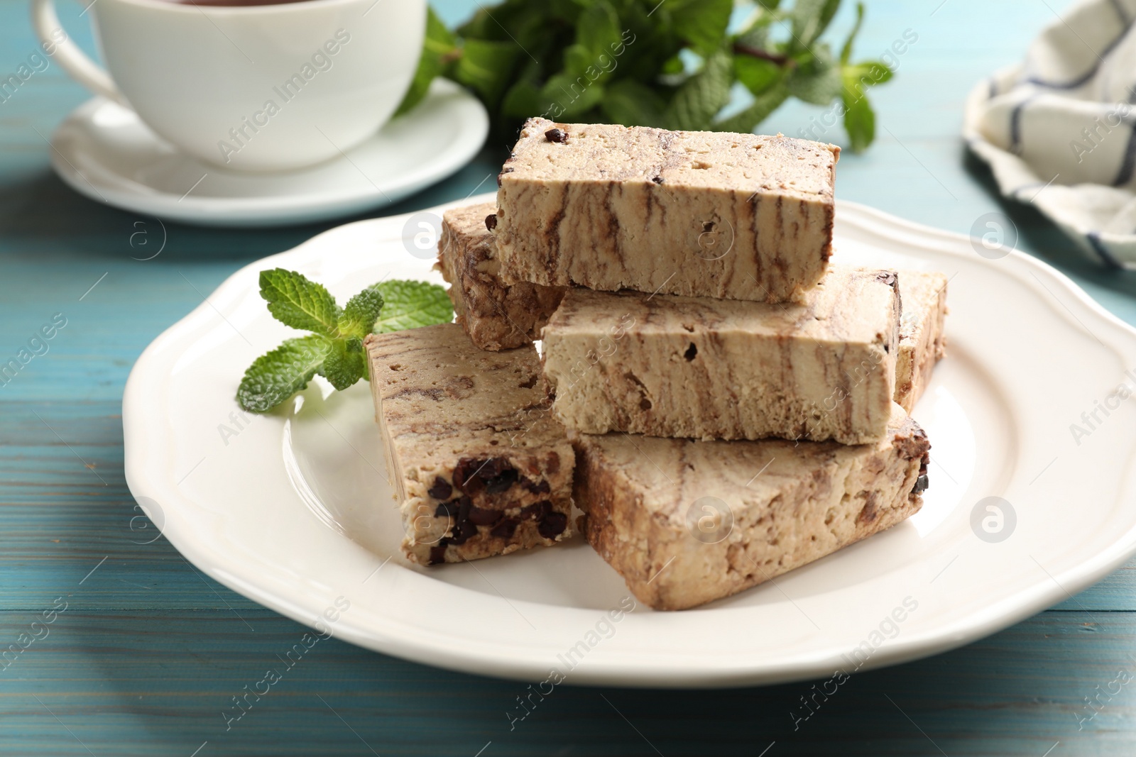 Photo of Pieces of tasty chocolate halva and mint on light blue wooden table, closeup