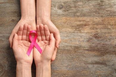 Photo of Women holding pink ribbon on wooden background, top view. Cancer awareness