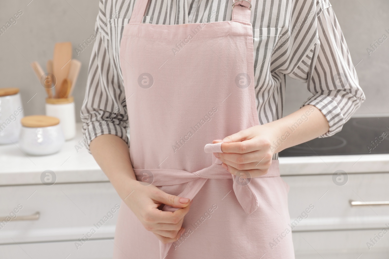 Photo of Woman putting on pink apron in kitchen , closeup