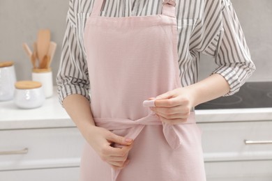 Photo of Woman putting on pink apron in kitchen , closeup