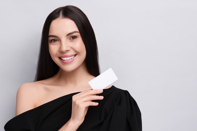 Happy woman holding blank business card on light grey background. Space for text