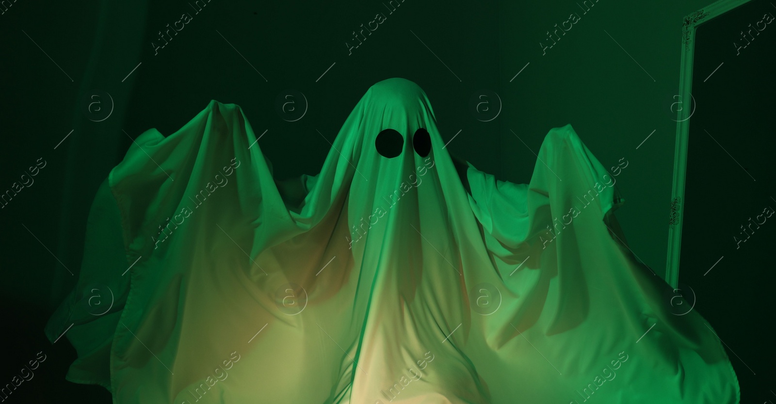 Photo of Creepy ghost. Woman covered with sheet in green light