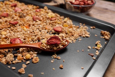 Photo of Making granola. Baking tray with mixture of oat flakes, other ingredients and spoon on table, closeup