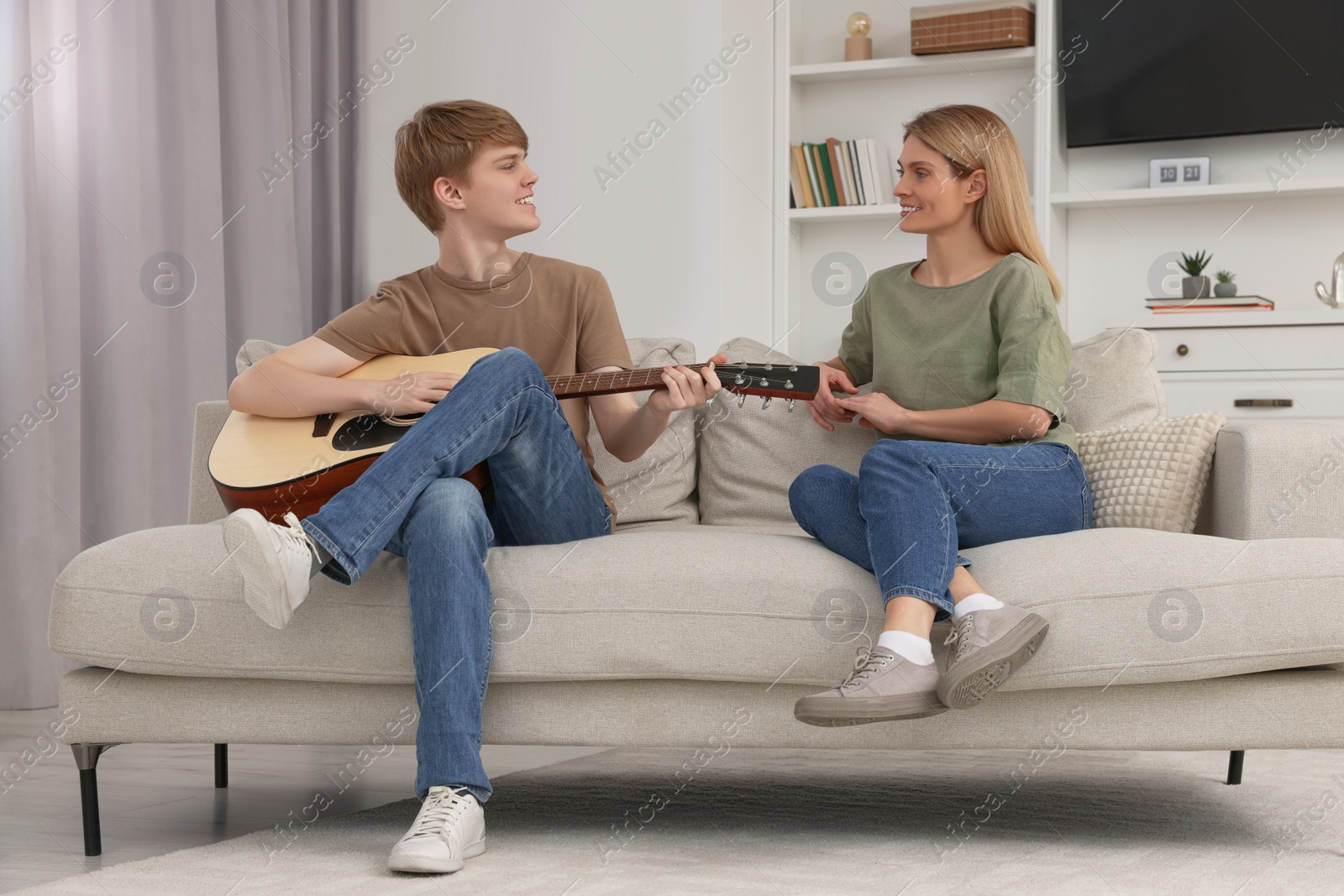 Photo of Teenage son playing guitar for his mother in living room