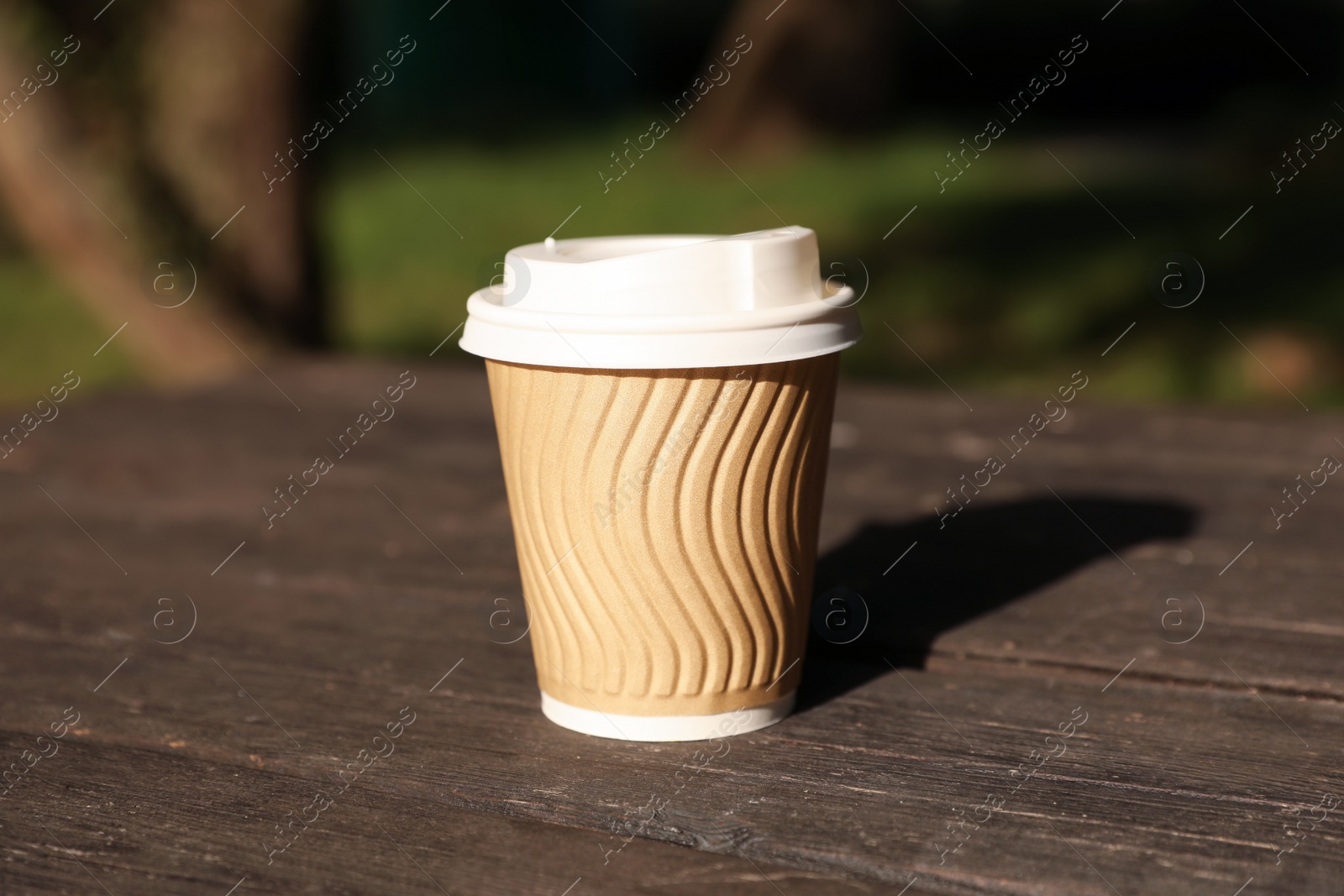 Photo of Paper cup on wooden table outdoors. Coffee to go