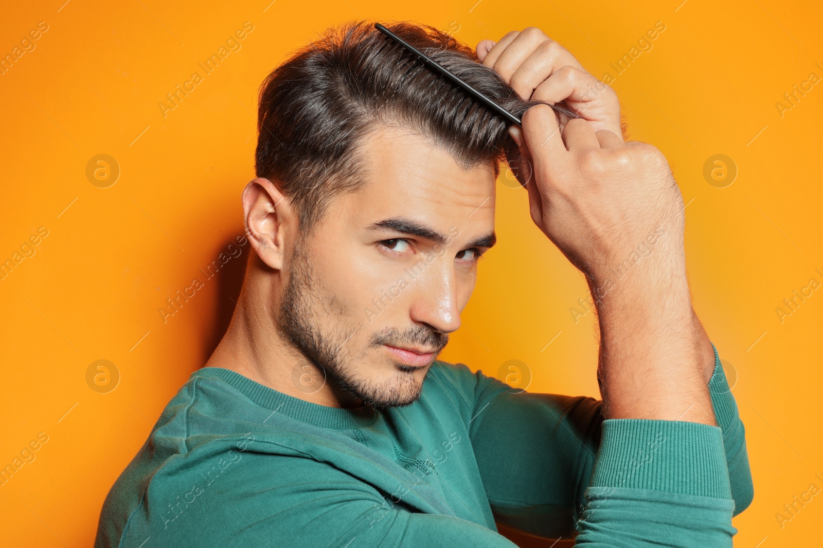 Photo of Young man with comb posing on color background. Trendy hairstyle