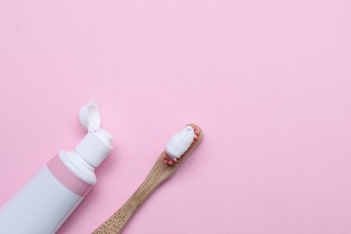 Photo of Brush with toothpaste and tube on pink background, flat lay. Space for text