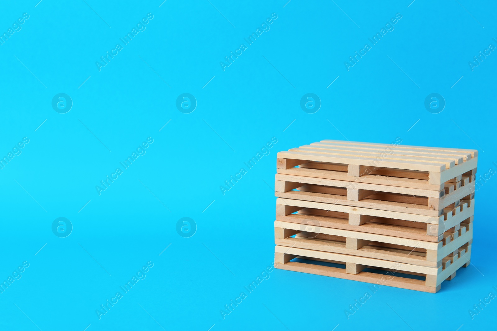 Photo of Stack of wooden pallets on light blue background, space for text