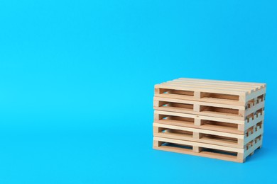 Stack of wooden pallets on light blue background, space for text