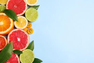 Photo of Fresh juicy citrus fruits with green leaves on light blue background, flat lay. Space for text