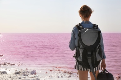 Woman with backpack on coast of pink lake