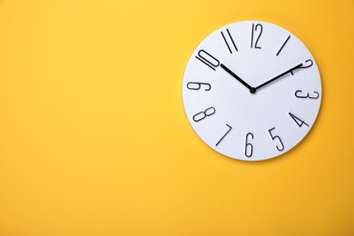 Modern clock on yellow background, top view. Space for text