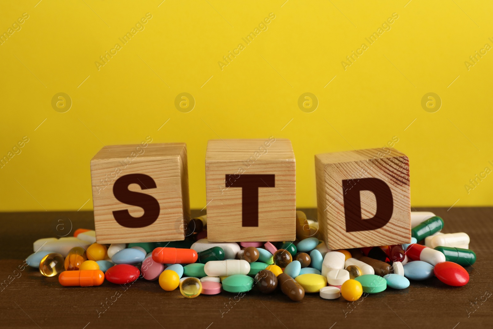 Photo of Abbreviation STD made with cubes and pills on wooden table against yellow background