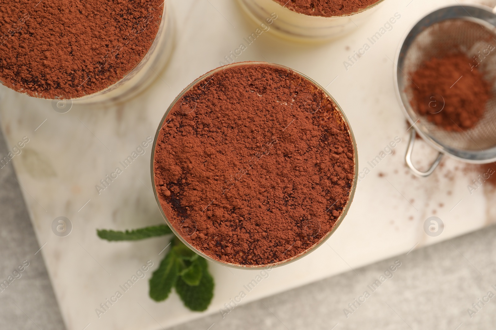 Photo of Delicious tiramisu in glasses and mint on grey textured table, top view