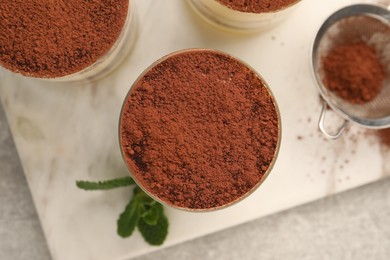 Photo of Delicious tiramisu in glasses and mint on grey textured table, top view