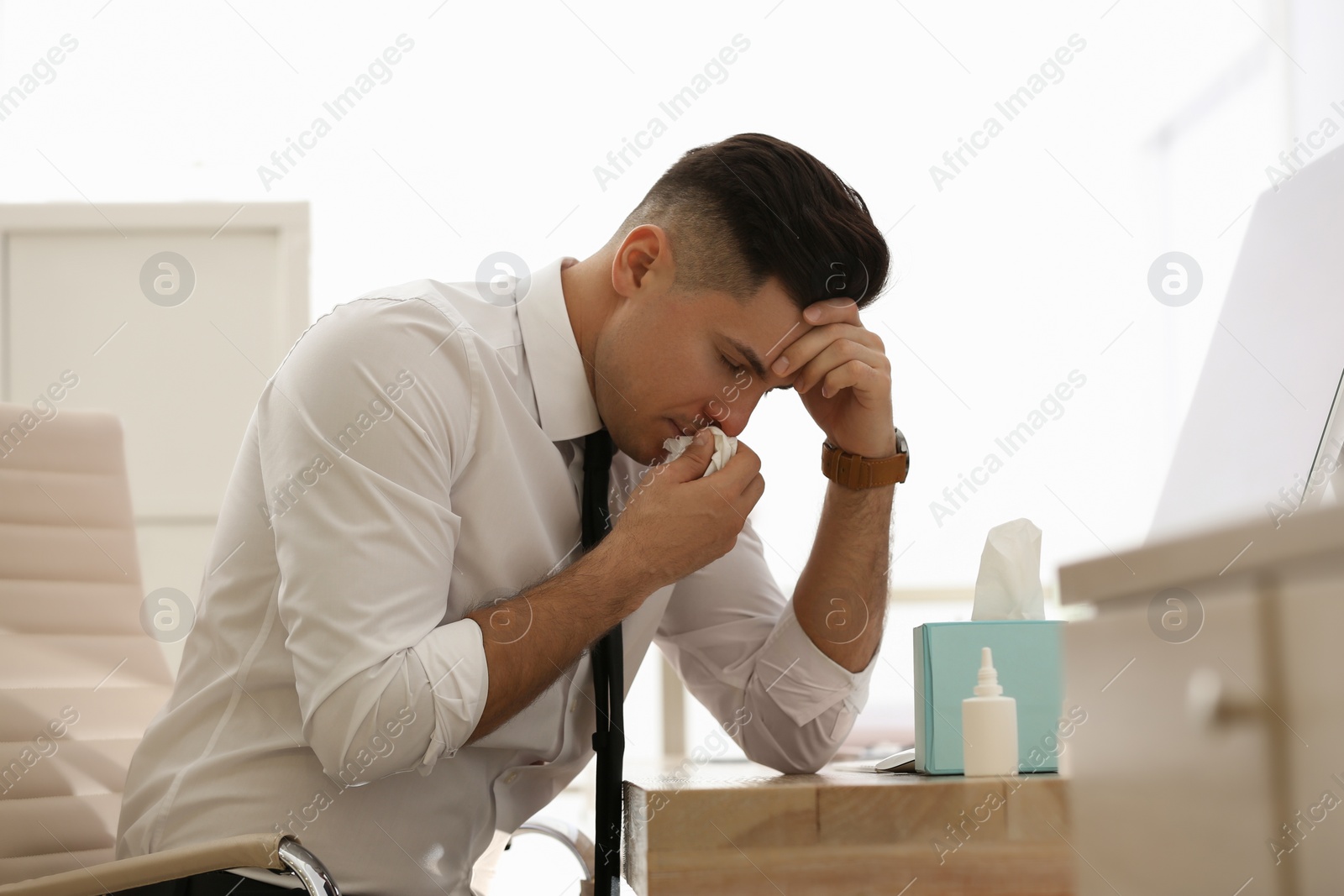 Photo of Ill businessman at table with nasal spray and box of paper tissues in office