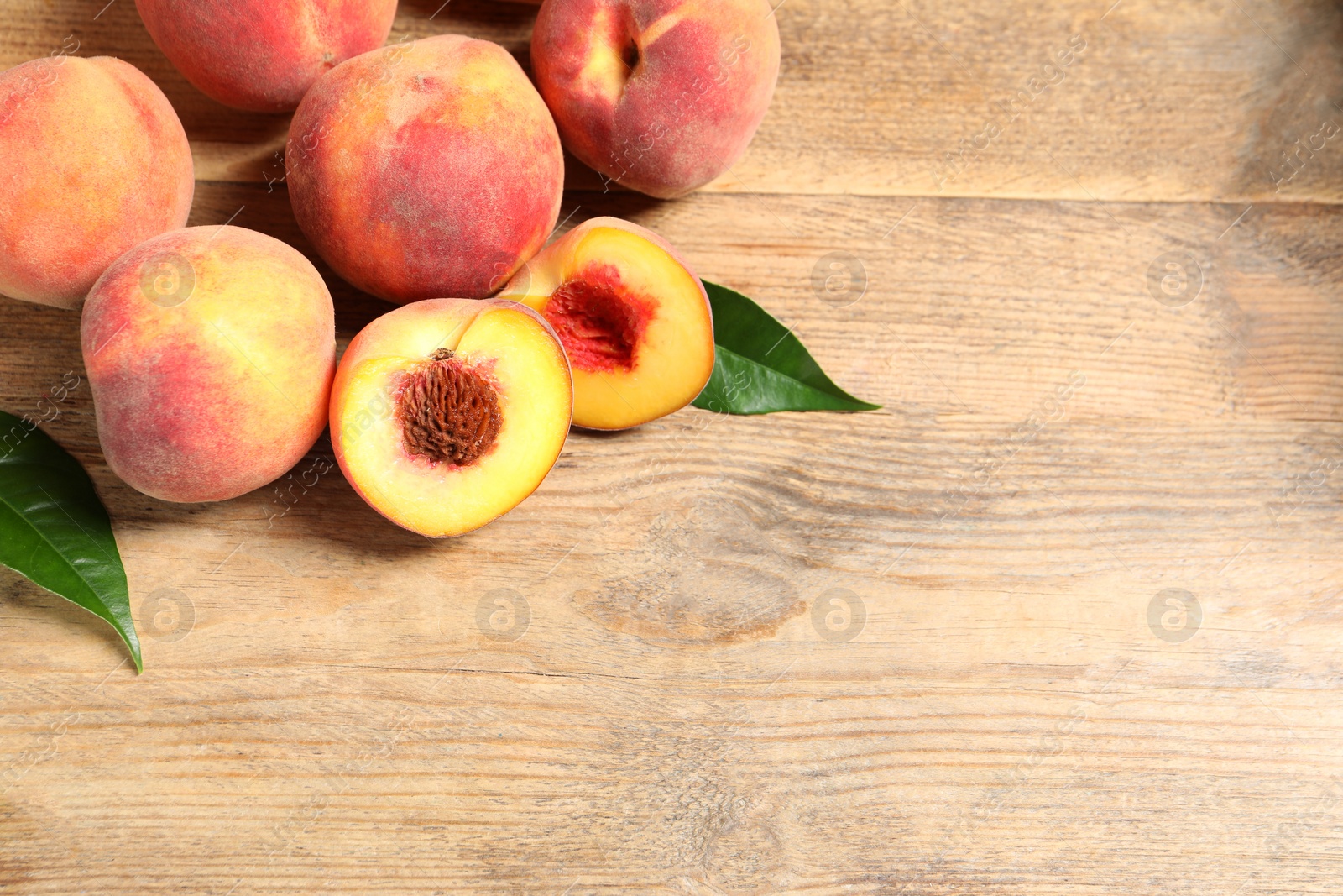 Photo of Cut and whole fresh ripe peaches with green leaves on wooden table. Space for text