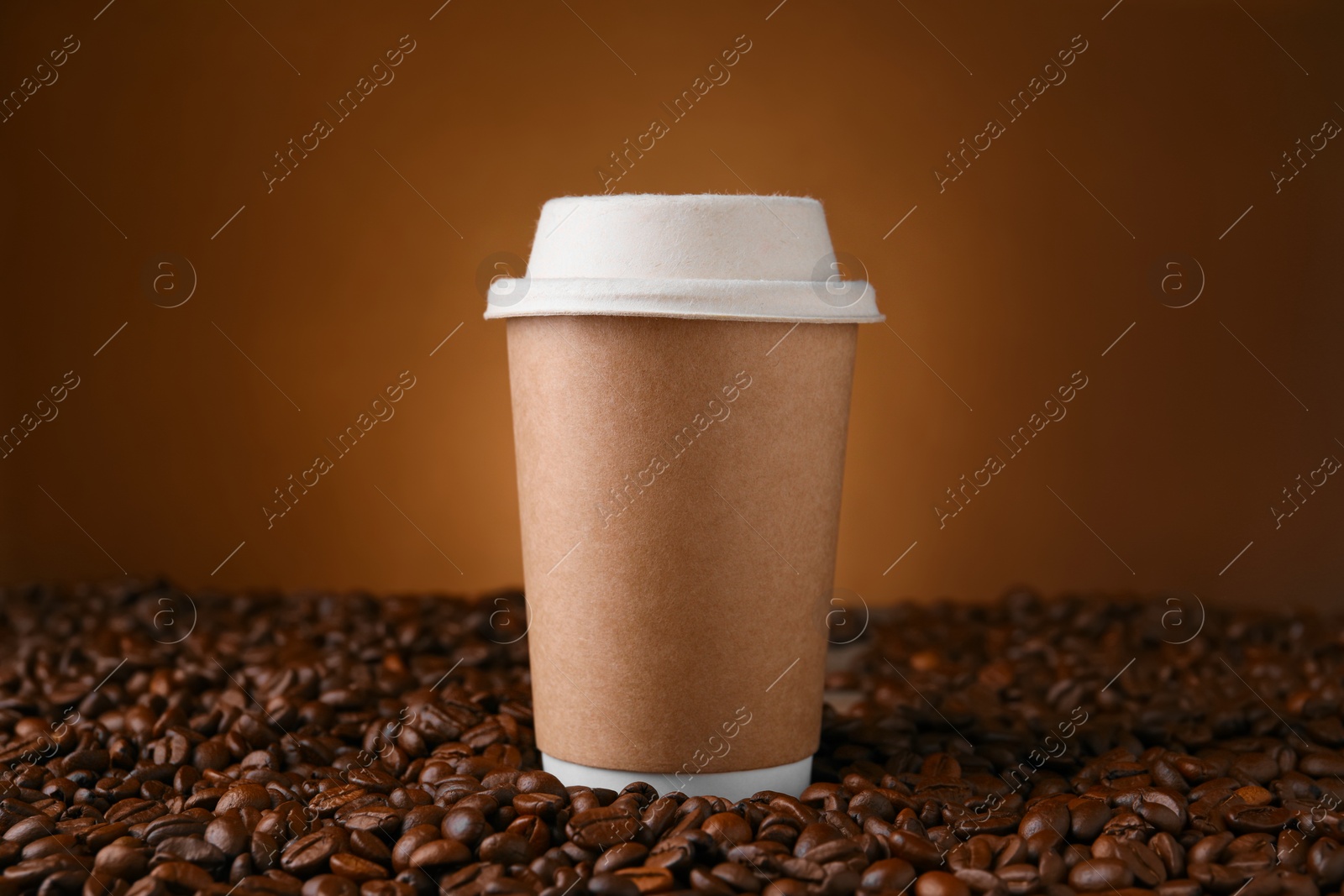 Photo of Coffee to go. Paper cup on roasted beans against brown background