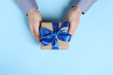 Photo of Man holding gift box with bow on light blue background, top view
