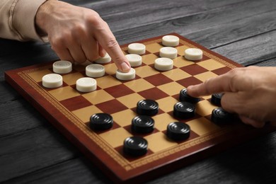 Photo of Man playing checkers with partner at black wooden table, closeup