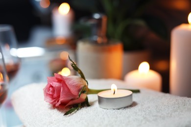 Photo of Rose and burning candle on towel, closeup. Romantic bath