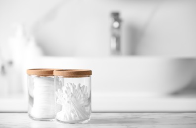 Photo of Glass jars with cotton pads and swabs on white countertop in bathroom. Space for text