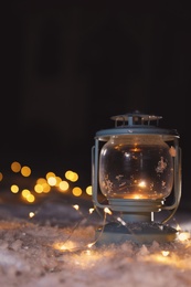 Photo of Lantern with burning candle and Christmas lights on white snow outdoors