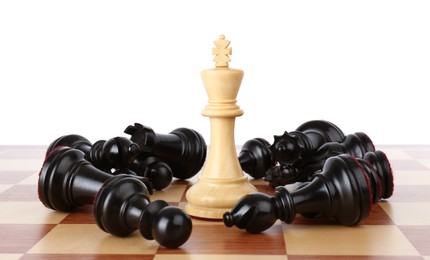 Photo of King among fallen black chess pieces on wooden board against white background