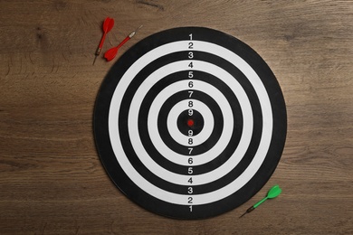 Dart board with color arrows on wooden background, top view