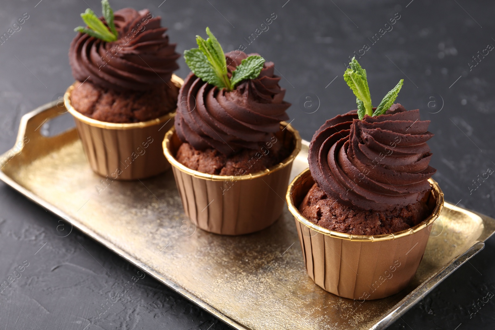 Photo of Delicious chocolate cupcakes with mint on black textured table, closeup