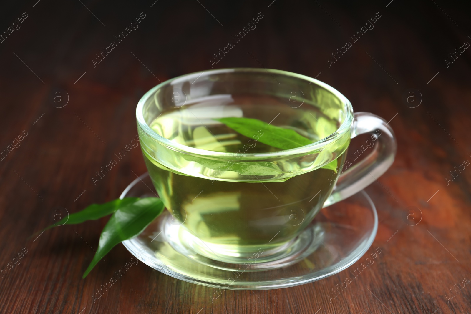 Photo of Cup of aromatic green tea and leaves on wooden table